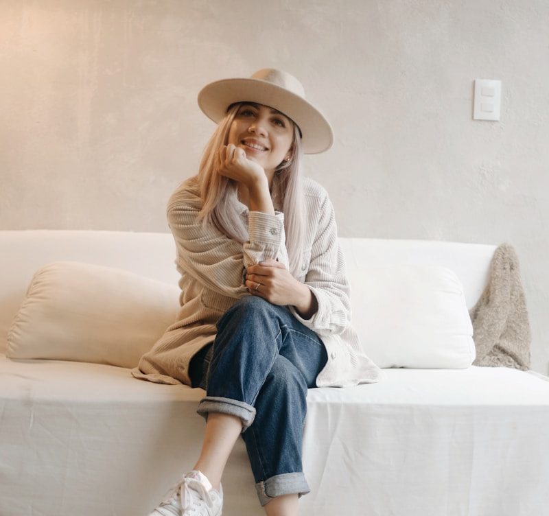 woman in white long sleeve shirt and blue denim jeans sitting on white couch